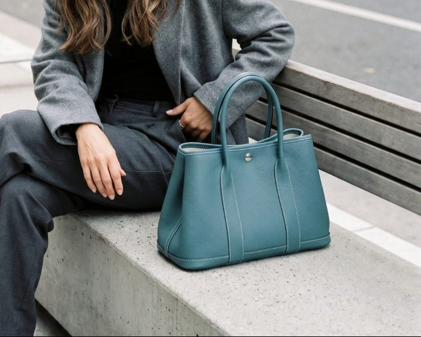 A woman sitting next to a blue leather tote bag with double top handles and a snap button closure from the Bella Dove Portofino collection.