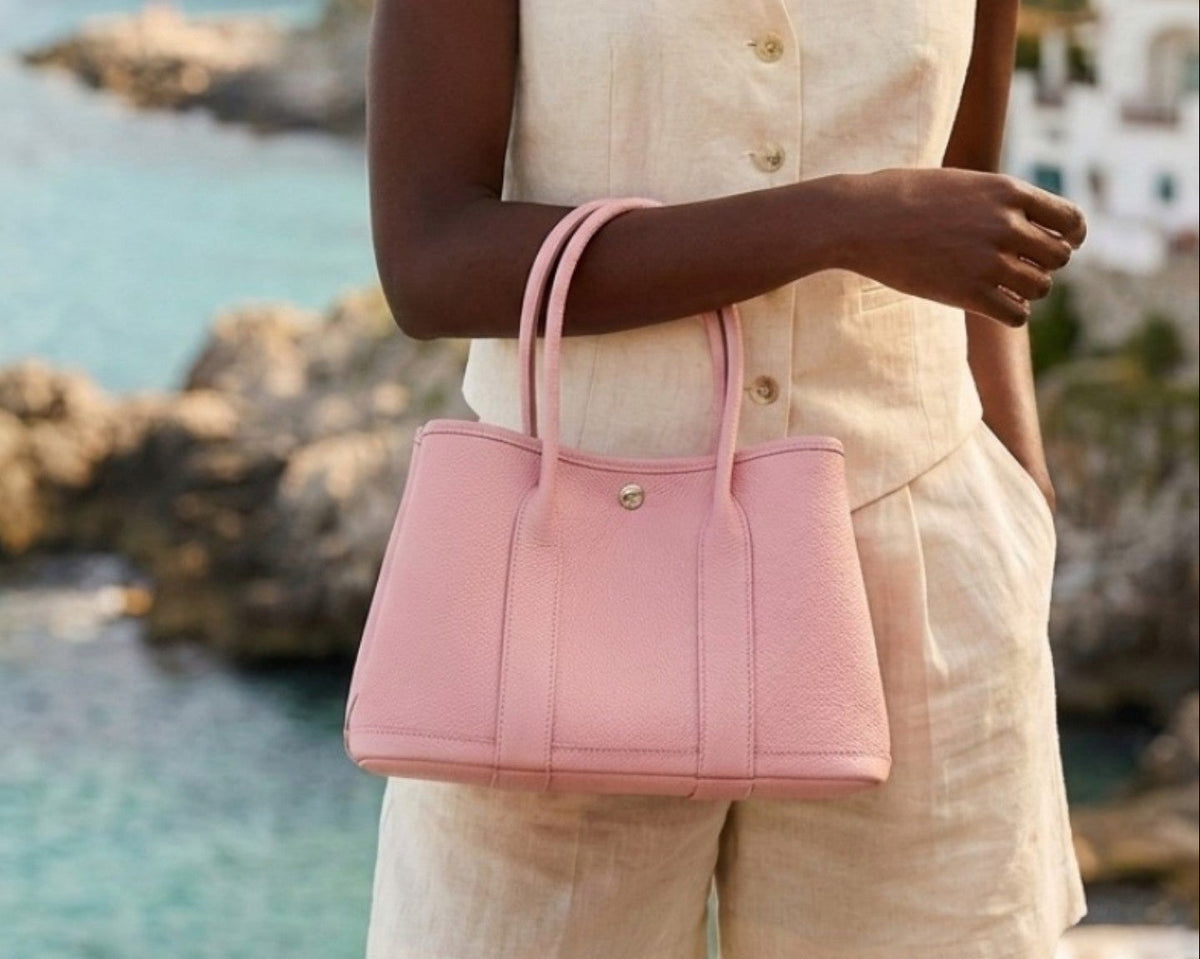 A woman wearing a light pink leather tote bag with double top handles and a snap button closure from the Bella Dove Portofino collection.